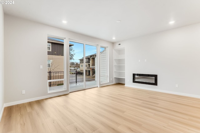 unfurnished living room with a glass covered fireplace, baseboards, and light wood finished floors