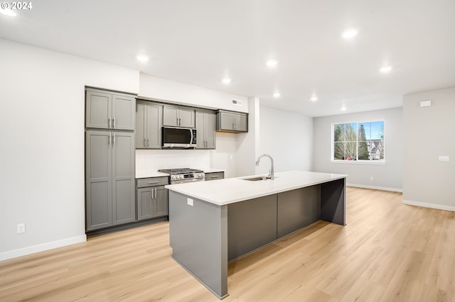 kitchen with stainless steel appliances, light countertops, gray cabinetry, a kitchen island with sink, and a sink