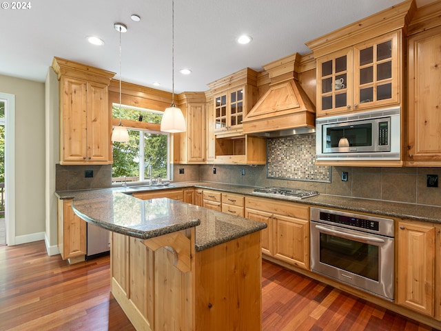 kitchen with stainless steel appliances, dark wood-type flooring, a kitchen island, decorative light fixtures, and dark stone countertops