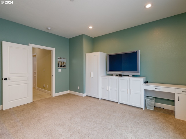 unfurnished bedroom with built in desk and light colored carpet