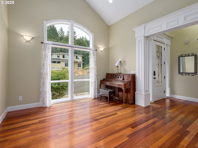 living area with high vaulted ceiling, baseboards, and wood finished floors