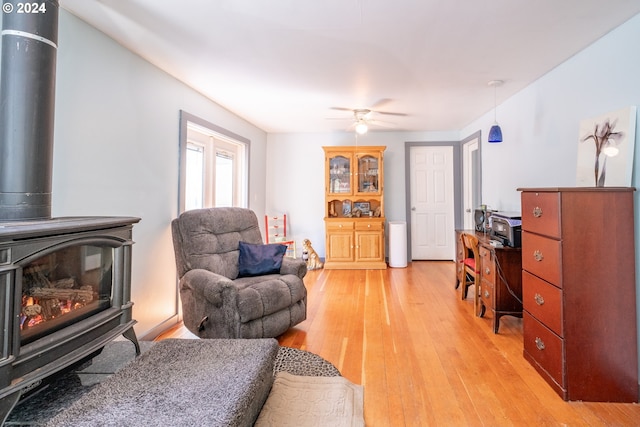 living room with light hardwood / wood-style floors, ceiling fan, and a wood stove