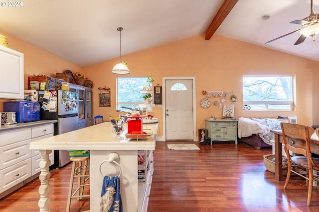 kitchen featuring dark wood-type flooring, decorative light fixtures, a kitchen bar, white cabinetry, and vaulted ceiling with beams