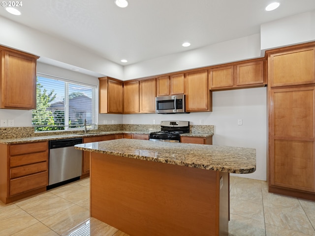 kitchen with a kitchen island, stainless steel appliances, light tile floors, and light stone counters