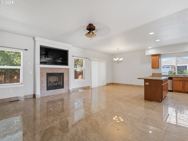 unfurnished living room featuring ceiling fan with notable chandelier, sink, a tiled fireplace, and light tile floors