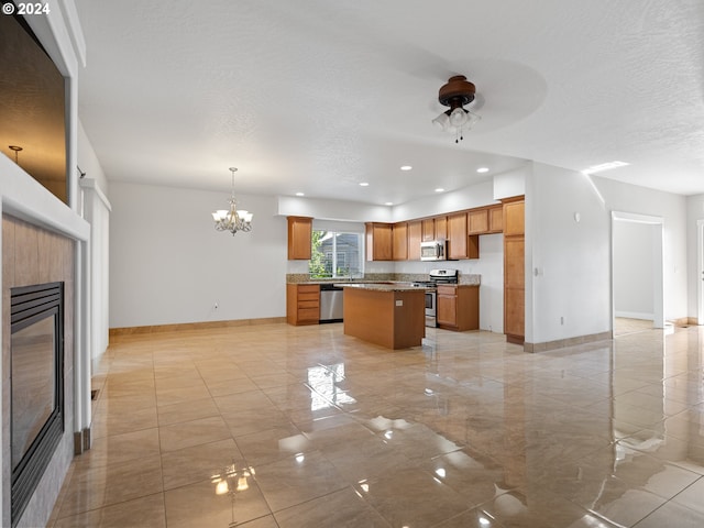 kitchen with decorative light fixtures, a fireplace, ceiling fan with notable chandelier, stainless steel appliances, and a kitchen island