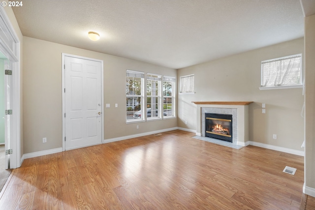 unfurnished living room with light hardwood / wood-style floors, a textured ceiling, and a tiled fireplace