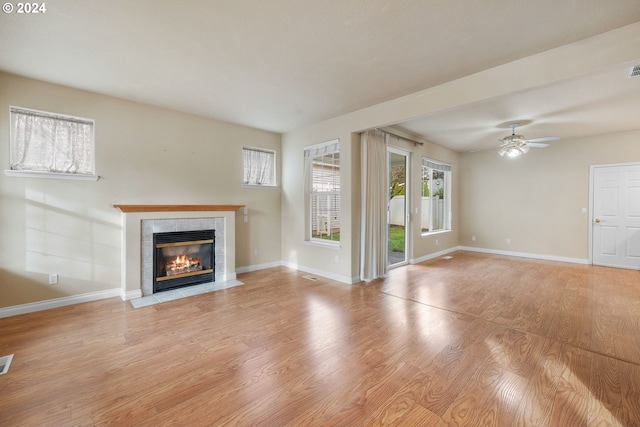 unfurnished living room with ceiling fan, a tile fireplace, and light hardwood / wood-style flooring