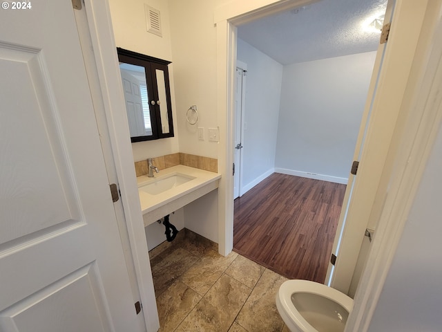 bathroom with toilet, a textured ceiling, wood-type flooring, and sink