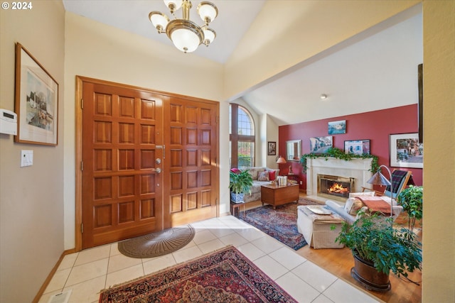 tiled foyer entrance featuring a high end fireplace, vaulted ceiling, and a chandelier