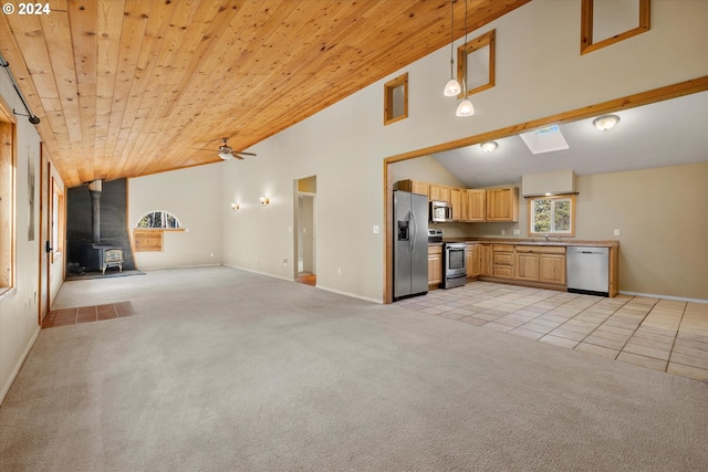 unfurnished living room with wood ceiling, a wood stove, light carpet, ceiling fan, and lofted ceiling with skylight