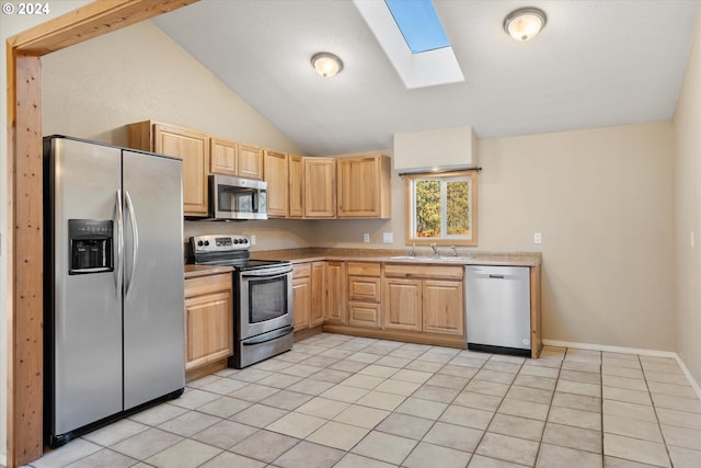 kitchen featuring light brown cabinets, appliances with stainless steel finishes, light tile patterned flooring, vaulted ceiling with skylight, and sink