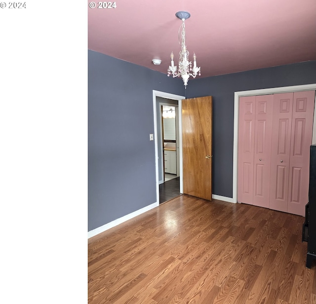 unfurnished bedroom featuring hardwood / wood-style floors, an inviting chandelier, and a closet