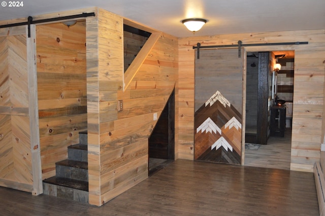 corridor with a baseboard heating unit, a barn door, dark hardwood / wood-style floors, and wooden walls