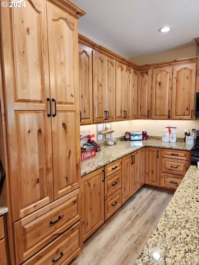 kitchen with light hardwood / wood-style floors, light stone counters, and black appliances