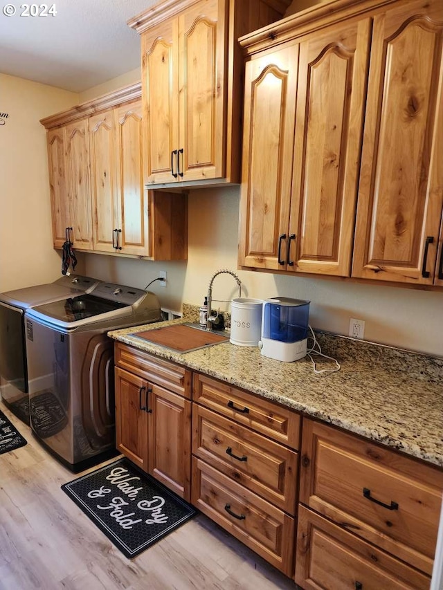 clothes washing area with cabinets, light wood-type flooring, sink, and separate washer and dryer