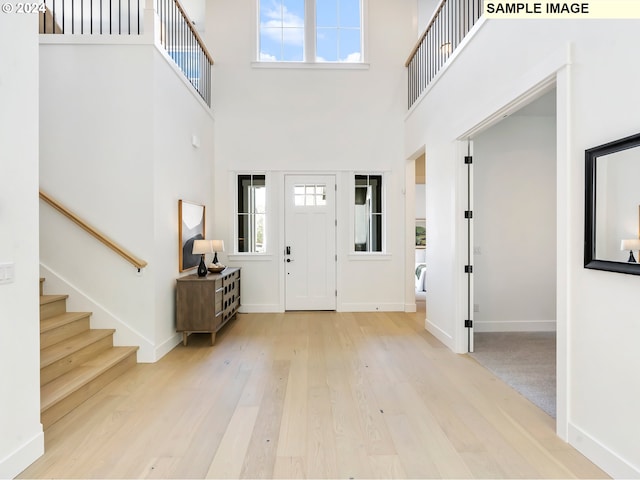 foyer featuring stairs, a towering ceiling, baseboards, and wood finished floors