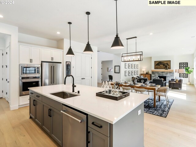 kitchen with appliances with stainless steel finishes, a stone fireplace, sink, light hardwood / wood-style floors, and decorative light fixtures