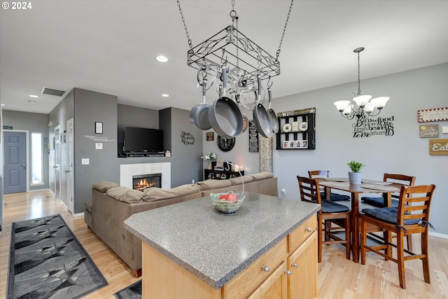 kitchen with a center island, light wood-type flooring, a tiled fireplace, light brown cabinets, and a chandelier