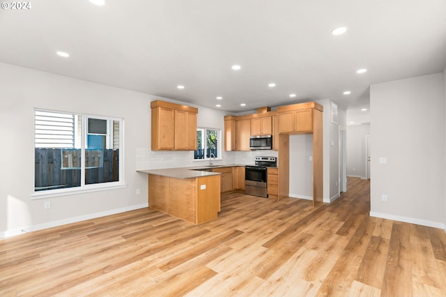 kitchen featuring light wood-type flooring, stainless steel appliances, kitchen peninsula, sink, and tasteful backsplash