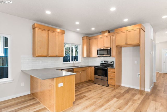 kitchen with light hardwood / wood-style floors, kitchen peninsula, tasteful backsplash, appliances with stainless steel finishes, and sink