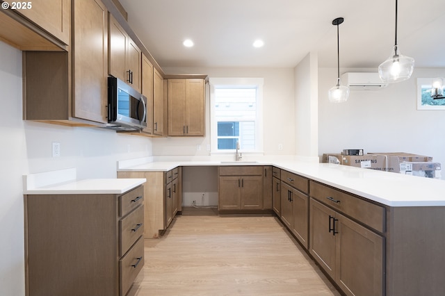 kitchen with an AC wall unit, sink, hanging light fixtures, kitchen peninsula, and plenty of natural light