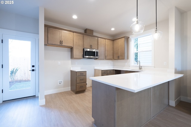 kitchen with sink, decorative light fixtures, light hardwood / wood-style floors, and kitchen peninsula