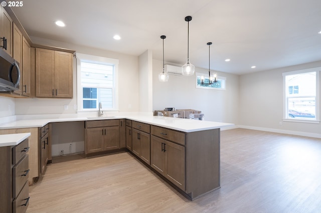 kitchen with decorative light fixtures, sink, a wall mounted AC, kitchen peninsula, and plenty of natural light