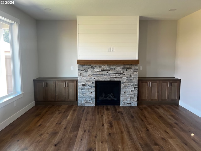 unfurnished living room featuring a stone fireplace, a wealth of natural light, and dark wood-type flooring