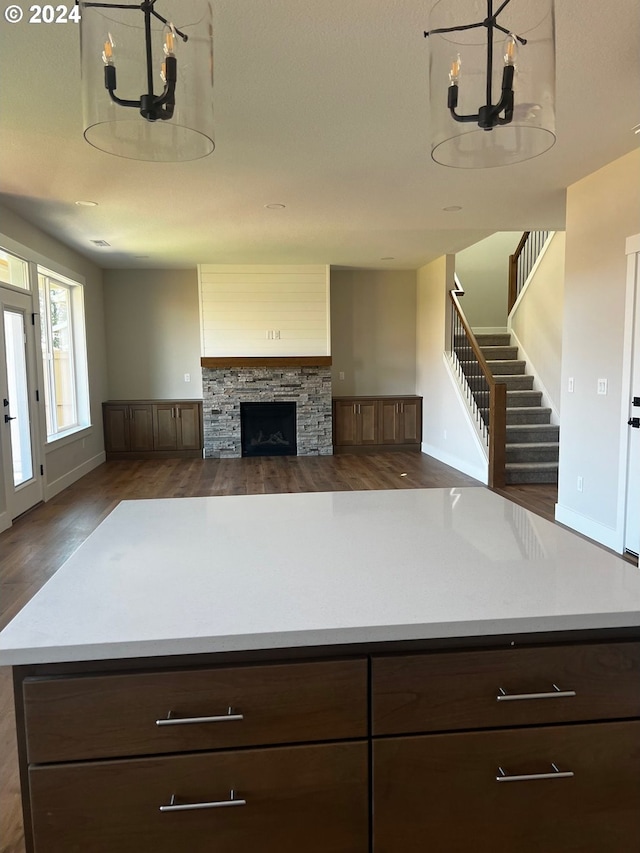 kitchen with dark hardwood / wood-style floors, a stone fireplace, dark brown cabinetry, and a chandelier