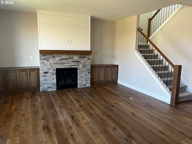 unfurnished living room featuring a stone fireplace and dark hardwood / wood-style floors