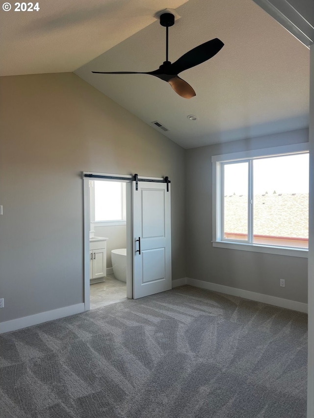 unfurnished bedroom featuring light carpet, ensuite bath, vaulted ceiling, ceiling fan, and a barn door