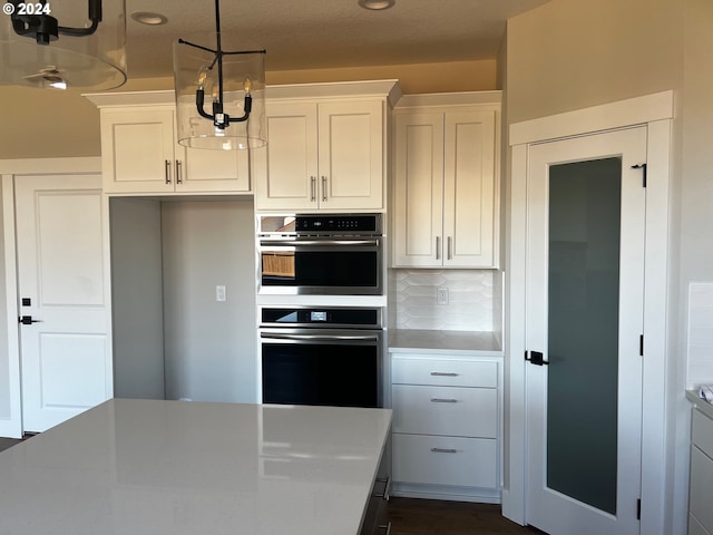 kitchen featuring white cabinets, decorative backsplash, stainless steel double oven, and hanging light fixtures