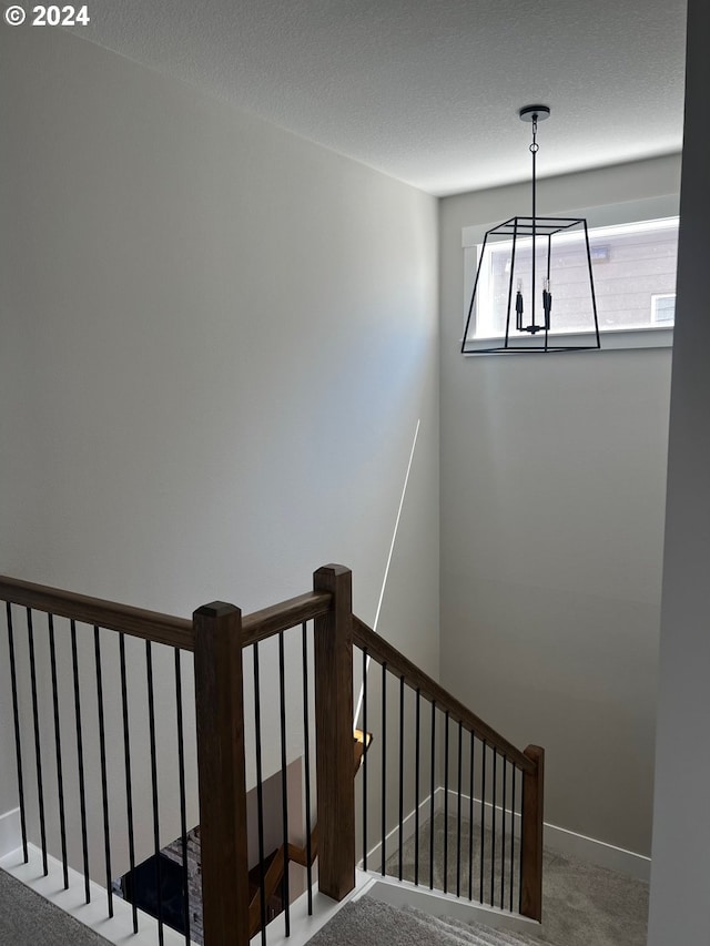 stairway with carpet flooring, a textured ceiling, and a chandelier