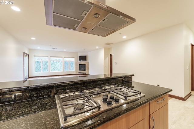 kitchen with a tile fireplace, stainless steel gas stovetop, and dark stone counters