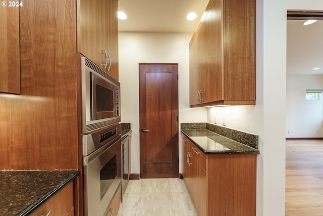 kitchen featuring stainless steel appliances, dark stone counters, and light wood-type flooring