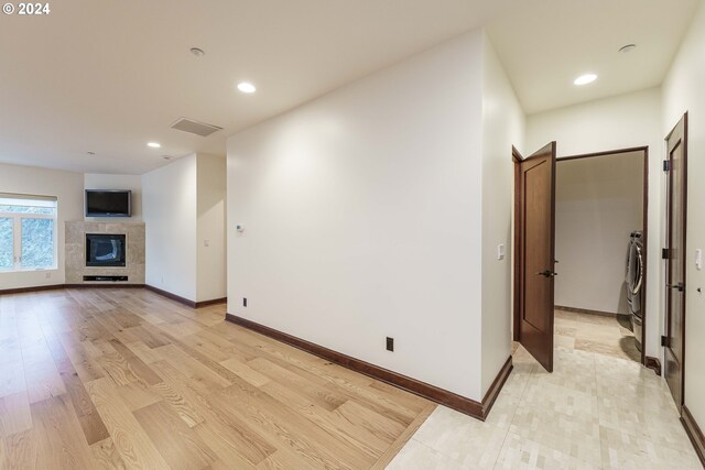 unfurnished living room with a tiled fireplace, light wood-type flooring, and washer / clothes dryer