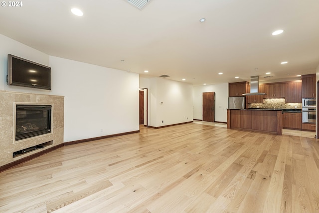 unfurnished living room with a tiled fireplace and light wood-type flooring