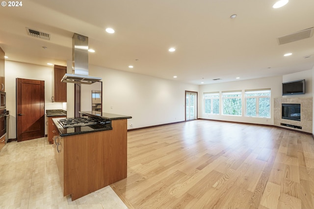 kitchen with a tile fireplace, island range hood, stainless steel gas cooktop, a kitchen island, and light hardwood / wood-style flooring