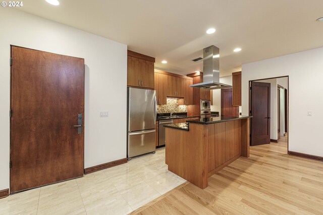 kitchen with stainless steel appliances, a kitchen bar, light wood-type flooring, decorative backsplash, and island range hood