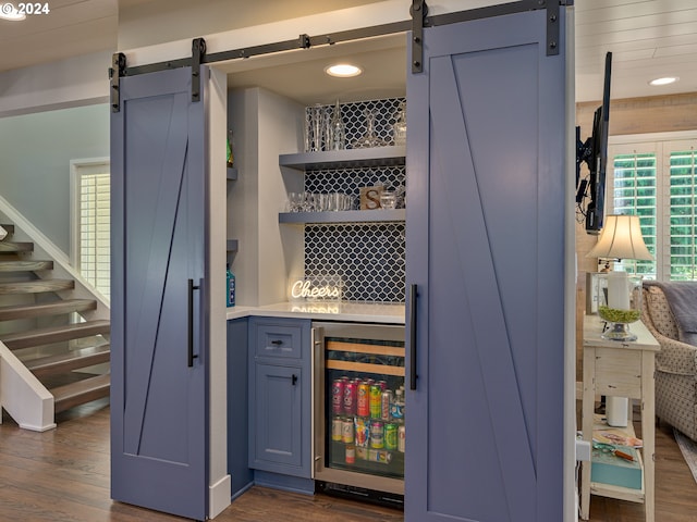 bar with dark wood-type flooring, wine cooler, and a barn door