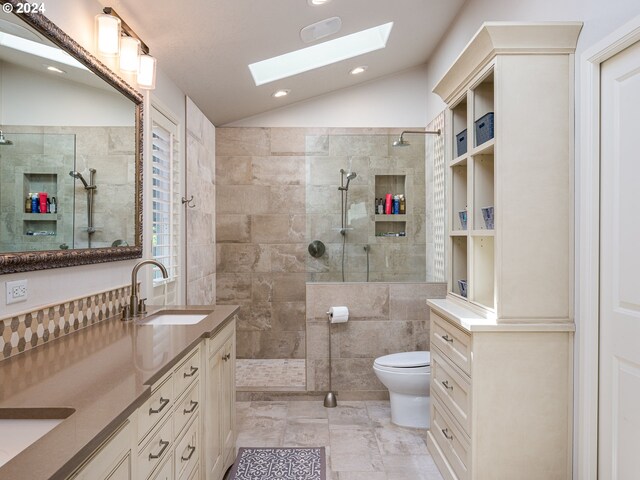 bathroom featuring a tile shower, vaulted ceiling with skylight, vanity, and toilet