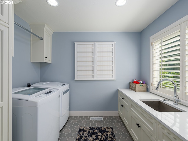 clothes washing area with washing machine and dryer, sink, dark tile patterned flooring, and cabinets