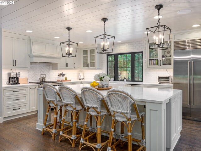 kitchen featuring dark hardwood / wood-style flooring, stainless steel built in fridge, hanging light fixtures, premium range hood, and a kitchen island