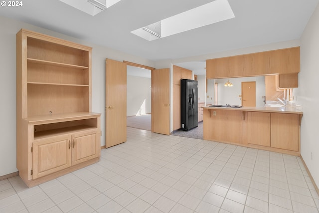 kitchen featuring kitchen peninsula, a kitchen bar, light brown cabinetry, a skylight, and black fridge