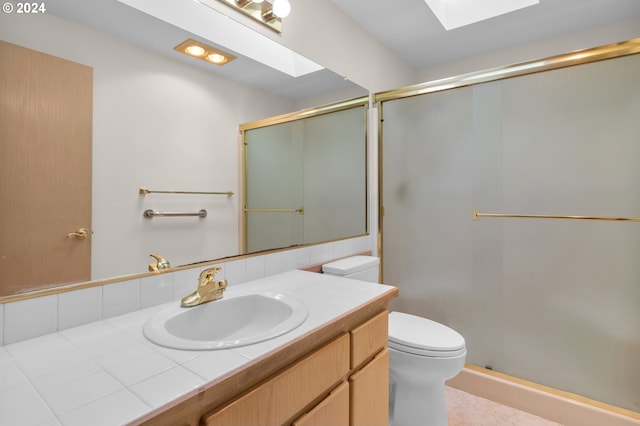 bathroom with a shower with door, toilet, vanity, and a skylight