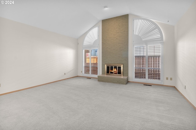 unfurnished living room with a brick fireplace, light colored carpet, plenty of natural light, and vaulted ceiling