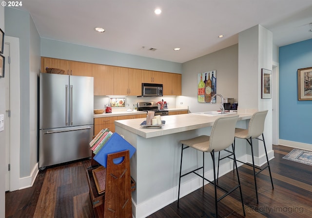 kitchen with stainless steel appliances, sink, dark hardwood / wood-style floors, kitchen peninsula, and a breakfast bar