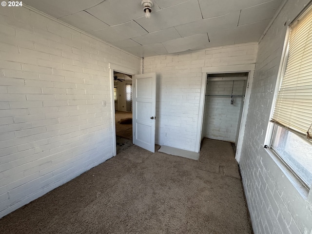 unfurnished bedroom with brick wall, multiple windows, and carpet floors