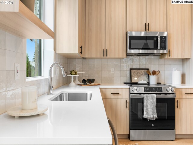 kitchen featuring sink, appliances with stainless steel finishes, light brown cabinets, backsplash, and light hardwood / wood-style flooring